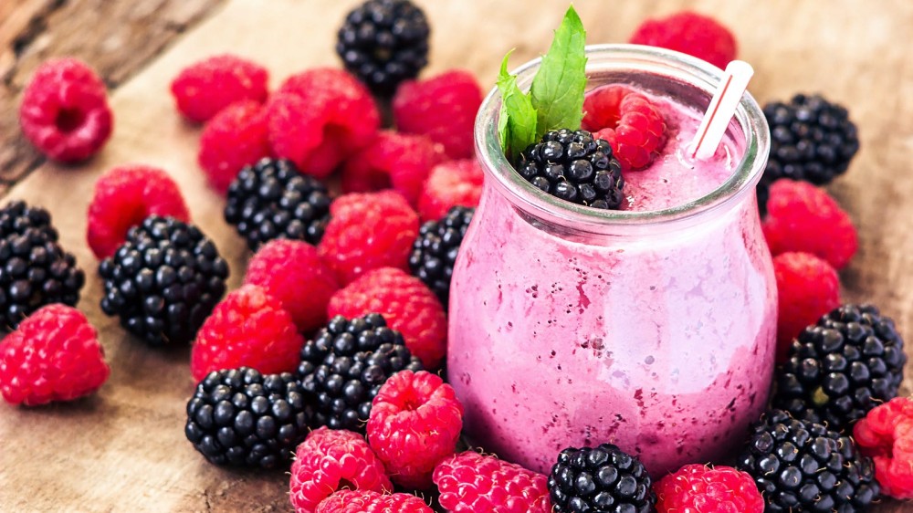 Fresh blackberries and raspberries next to a smoothie glass with a freshly made smoothie.