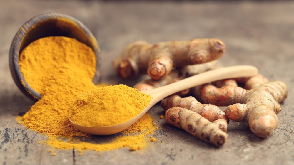 Turmeric root and ground turmeric on a wooden background.