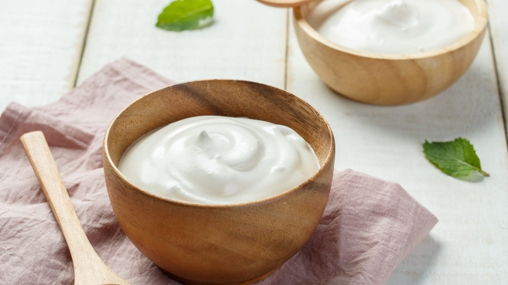 Two bowls of Greek yogurt with a wooden spoon along side it. 