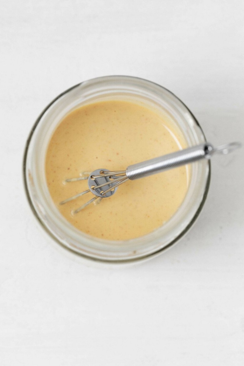 A Dijon lemon tahini dressing is being whisked in a small, round, Pyrex bowl.