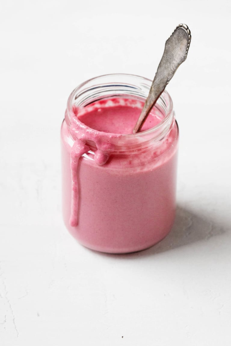 A glass jar holds a bright pink tahini beet dressing and a mixing spoon.